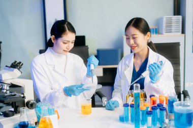 Yüksek teknolojili bir laboratuvarda, mikro pipetler kullanarak biyokimyasal örnekleri analiz eden ve hassas bir şekilde ileri düzey tıbbi araştırmalar yapan iki Asyalı kadın bilim adamı..