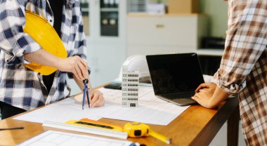 Çalışma ve tablet hakkında konuşan iki meslektaşım, ofisteki inşaat alanında mimari projeli dizüstü bilgisayar.