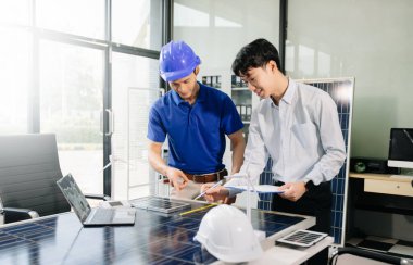 İki Asyalı mühendis, dizüstü bilgisayar kullanarak, modern ofis ortamında yenilik ve sürdürülebilirliği tartışan bir güneş enerjisi ve rüzgar enerjisi projesinde işbirliği yapıyorlar. Temiz enerji, takım çalışması ve ilerleme