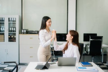 Asyalı mutlu iş kadınları dizüstü bilgisayar ve tablet kullanıyorlar. Takım çalışması, finansal pazarlama ekibi, modern ofis odasında otururken. 