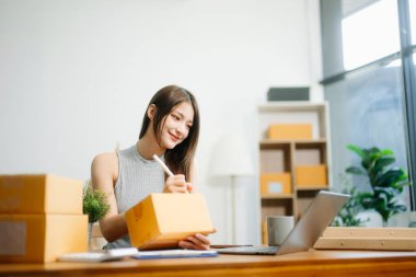 Genç işyeri sahibi kadın paket kutusunu hazırla ve tablet, dizüstü bilgisayar alışverişi online konsept üzerinden müşteriye teslimat için çevrimiçi kontrol yap.