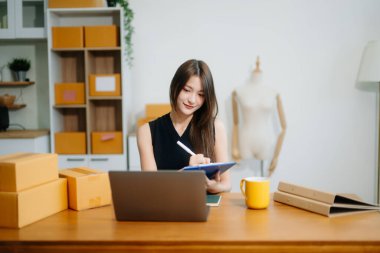 Genç işyeri sahibi kadın paket kutusunu hazırla ve tablet, dizüstü bilgisayar alışverişi online konsept üzerinden müşteriye teslimat için çevrimiçi kontrol yap.