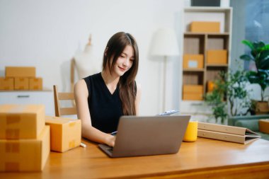 Genç işyeri sahibi kadın paket kutusunu hazırla ve tablet, dizüstü bilgisayar alışverişi online konsept üzerinden müşteriye teslimat için çevrimiçi kontrol yap.