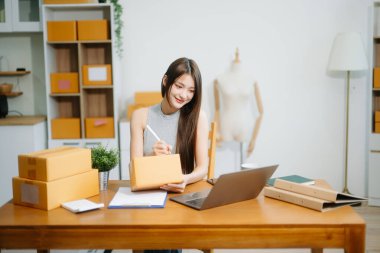 Genç işyeri sahibi kadın paket kutusunu hazırla ve tablet, dizüstü bilgisayar alışverişi online konsept üzerinden müşteriye teslimat için çevrimiçi kontrol yap.