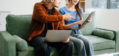 Kadın ve erkek rahat bir oturma odasında uzaktan çalışmaktan zevk alırlar. Kahve içip sohbet ederken dizüstü bilgisayar kullanırlar..  