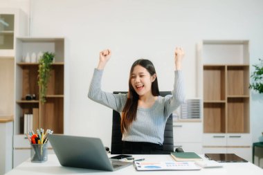 Genç, güzel bir kadın, modern ofisteki çalışan beyaz masada otururken tablet ve dizüstü bilgisayarda yazı yazıyor.