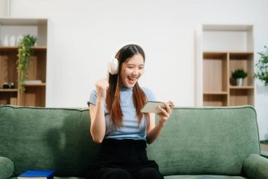 Genç Asyalı kadın kulaklıklardan müzik dinliyor ve iş fikri için günlük defterine not yazıyor..