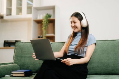 Genç Asyalı kadın evdeki kanepede akıllı telefon ve tablet kullanıyor.
