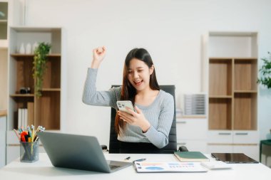 Genç ve güzel bir kadın, modern ofisin beyaz çalışma masasında otururken tablet ve dizüstü bilgisayarında yazıyor.