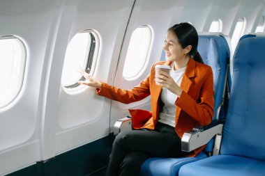 Çekici Asyalı kadın uçak yolcusu dizüstü bilgisayar ve tabletle kablosuz bağlantı kullanarak rahat koltukta oturuyor. Stil içinde seyahat et, zarafetle çalış..