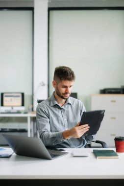 Ofis masasında tablet ve dizüstü bilgisayarla finans analizi üzerinde çalışan kendine güvenen bir iş adamı. İş, muhasebe ve profesyonel iş yeri kavramları için mükemmel.