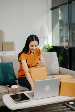 Startup small business SME, Entrepreneur owner woman using smartphone or tablet taking receive and checking online purchase shopping order to preparing pack product box. 