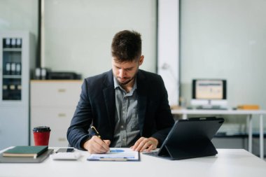 Ofis masasında tablet ve dizüstü bilgisayarla finans analizi üzerinde çalışan kendine güvenen bir iş adamı. İş, muhasebe ve profesyonel iş yeri kavramları için mükemmel.