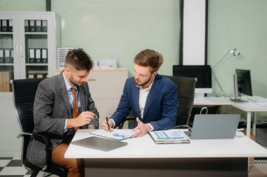 İki ofis arkadaşı, modern bir çalışma alanında yeni bir proje için fikir alışverişinde bulunuyor.                          