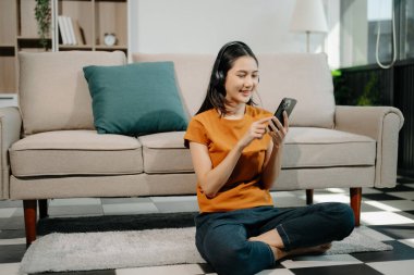 Genç Asyalı kadın evdeki kanepede otururken akıllı telefon ve tablet kullanıyor.