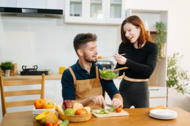 Neşeli çift taze sebzeler hazırlıyor, sağlıklı beslenmeyi kucaklıyor ve canlı bir mutfak ortamında takım çalışması yapıyorlar. Sağlıklı yaşam tarzı için mükemmel.