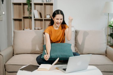 Kanepede oturan Asyalı kadın bilgisayarını kullanarak Finans ve Pazarlama 'yı yönetiyor.