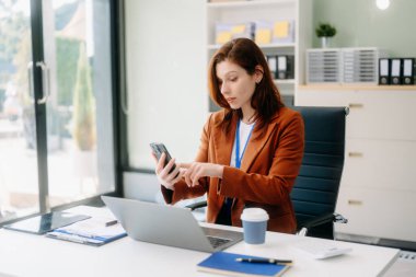 Kendine güvenen iş uzmanı, gülümseyen, dizüstü bilgisayarda yazan ve dijital tableti yaratıcı ofiste tutan çekici genç bir kadın.