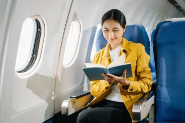 Çekici Asyalı kadın uçak yolcusu rahat koltukta oturup kitap okuyor.