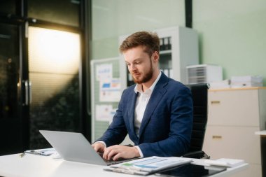 Ofiste dizüstü bilgisayarla çalışan genç bir iş adamı. İş, finans, muhasebe ve işyeri kavramları için mükemmel.