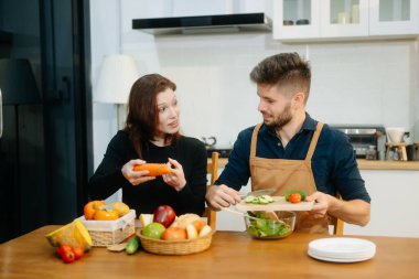 Neşeli çift taze sebzeler hazırlıyor, sağlıklı beslenmeyi kucaklıyor ve canlı bir mutfak ortamında takım çalışması yapıyorlar. Sağlıklı yaşam tarzı için mükemmel.