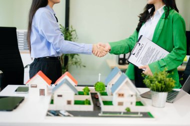 Mülk sektörünü dengelemek. Emlakçı müşteriyle ev tasarımı ve satın alma anlaşması hakkında tokalaşıyor. Modern ofiste model evler