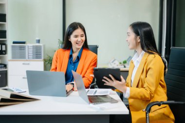 Businesswomen work and discuss their business plans. A woman employee explains and shows her colleague the results paper in modern office.