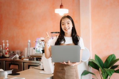 Başlangıçta küçük işletme sahibi başarılı bir kadındı. Kafede dizüstü bilgisayarla çalışıyor ve baş parmak işareti gösteriyordu..