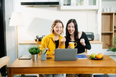 Beyaz kadınlar mutfak masasında oturmuş laptopla evden çalışıyorlar.. 