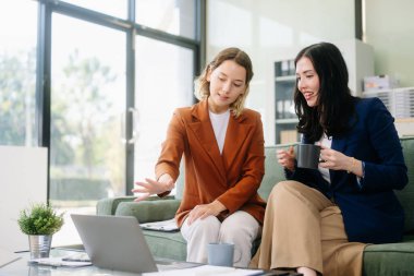 Profesyonel bir ofiste tabletle strateji kuran iki iş kadını. Bu modern işbirliği konseptiyle takım çalışmasını, liderliği ve yeniliği vurgula.