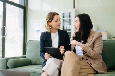 Profesyonel bir ofiste tabletle strateji kuran iki iş kadını. Bu modern işbirliği konseptiyle takım çalışmasını, liderliği ve yeniliği vurgula.