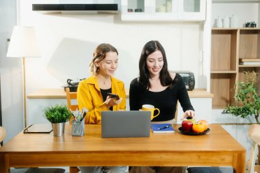 Beyaz kadınlar mutfak masasında oturup dizüstü bilgisayarlar ve akıllı telefonlar üzerinde çalışıyorlar.. 