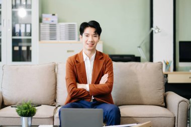 Asyalı girişimci şık bir ofisteki kanepede dizüstü bilgisayar kullanarak işine odaklandı..