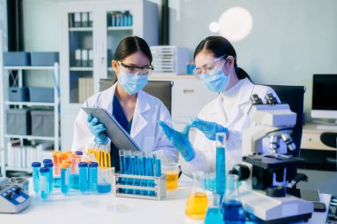 Yüz maskesi takmış genç Asyalı bilim adamları bir tıp laboratuarında araştırma araştırması yürütüyor.