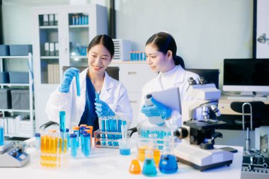 İki Asyalı kadın bilim adamı yüksek teknoloji laboratuvarında biyokimyasal örnekleri analiz ediyorlar, dijital tablet, mikro pipetler kullanıyorlar ve hassas bir tıbbi araştırma yapıyorlar..