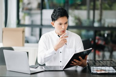 Asyalı işadamı, modern ofiste bir tablet üzerinde çalışmaktan stresli, sıkılmış ve aşırı düşünüyor.