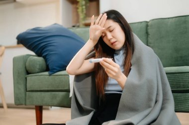 Kanepede battaniyeyle kaplanmış, grip belirtileri gösteren genç bir Asyalı kadın. Hastalık, sağlık ve iyileşme kavramı. Evde kal, sağlığına dikkat et.