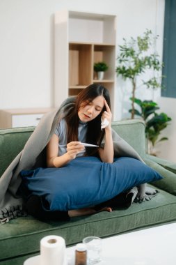 Kanepede battaniyeyle kaplanmış, grip belirtileri gösteren genç bir Asyalı kadın. Hastalık, sağlık ve iyileşme kavramı. Evde kal, sağlığına dikkat et.