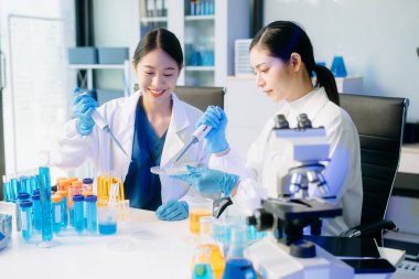 Yüksek teknolojili bir laboratuvarda, mikro pipetler kullanarak biyokimyasal örnekleri analiz eden ve hassas bir şekilde ileri düzey tıbbi araştırmalar yapan iki Asyalı kadın bilim adamı..