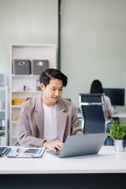 Genç işadamı ofiste dizüstü bilgisayarla çalışıyor.