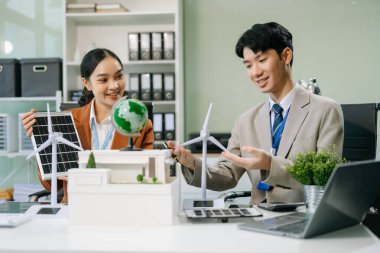 Masanın yanında duran bir grup iş adamı konut projesinden alınan bina modeline bakıyor. Yeşil iş şirketi ve Güneş Enerjisi Çevre Kenti Kavramı.