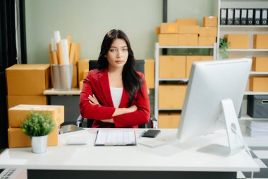 Asyalı iş kadını, çevrimiçi alışveriş konseptinde poz vererek, internet üzerinden teslimat için paketler hazırlıyor ve siparişleri kontrol ediyor. 