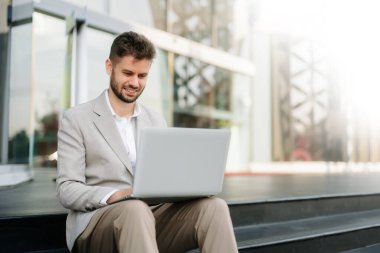 Başarılı iş adamı ofisin yakınında merdivenlerde dizüstü bilgisayarla çalışır.