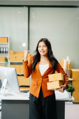 Mutlu girişimci Asyalı kadın ofiste teslimat için paketler hazırlıyor, el kol hareketi yapıyor. çevrimiçi alışveriş kavramı 