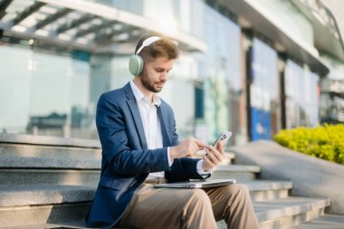 Kulaklık takan modern iş adamı, akıllı telefon ve dizüstü bilgisayar kullanıyor. İş, teknoloji ve yenilik temaları için idealdir. Kurumsal, profesyonel ve şehir yaşam tarzı kavramı.