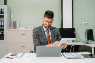 Ofis masasında tablet ve dizüstü bilgisayarla finans analizi üzerinde çalışan kendine güvenen bir iş adamı. İş, muhasebe ve profesyonel iş yeri kavramları için mükemmel.