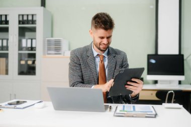 Ofis masasında tablet ve dizüstü bilgisayarla finans analizi üzerinde çalışan kendine güvenen bir iş adamı. İş, muhasebe ve profesyonel iş yeri kavramları için mükemmel..