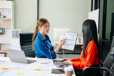 Asyalı iş arkadaşları dizüstü bilgisayar ve tablet kullanarak açıklama yapıyor. Takım çalışması, finansal pazarlama ekibi, modern ofis odasında otururken. 