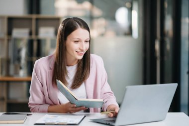 Ofiste otururken elinde defter olan kadın.