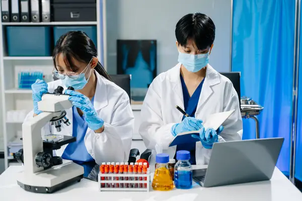 Laboratuar önlüklü bilim adamları, cam eşyalar üzerinde araştırma yapıyorlar ve modern, yüksek teknoloji laboratuvarında kimyasallarla çalışıyorlar.